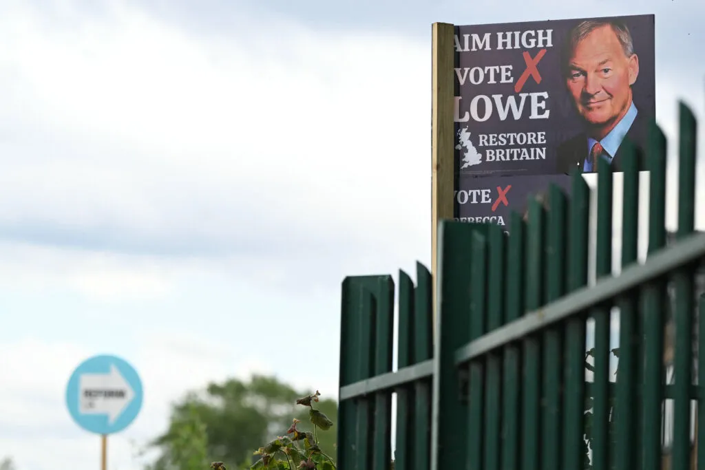 Affiche du parti Restore Britain devant une affiche de Reform UK